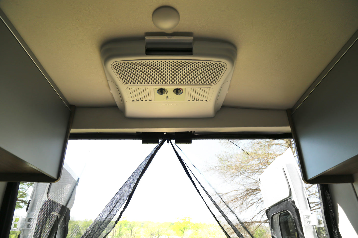 RV rental interior. Features a Dometic AC unit on the ceiling, overhead cabinets, and a zippered rear mesh screen for air flow.