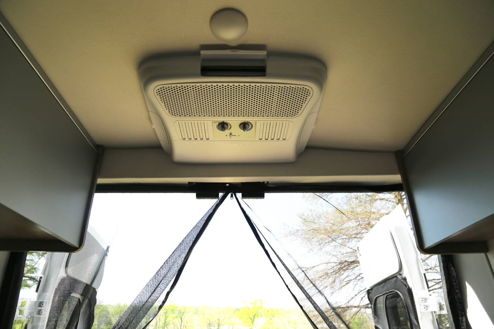 RV rental interior. Features a Dometic AC unit on the ceiling, overhead cabinets, and a zippered rear mesh screen for air flow.