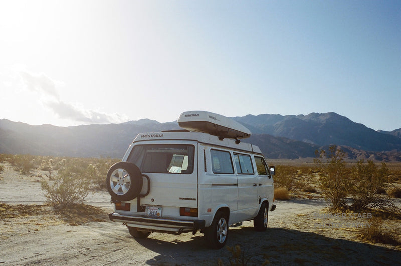 White Westfalia camper van with roof cargo box, parked in a sunny desert landscape with mountains; ideal RV rental. — photo 1