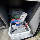 RV rental storage showing kitchen supplies (grater, measuring cup), First Aid kit, and Otter Box cooler for organized travel.