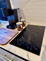 Compact kitchen area in an rv rental with a Keurig coffee maker, induction cooktop, and cutting board for efficient meal prep.