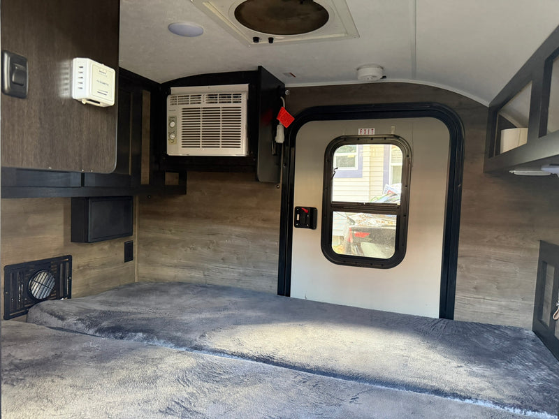 RV rental interior showing a sleeping area with gray blanket, mounted AC, Dometic thermostat, and exit door. — photo 7