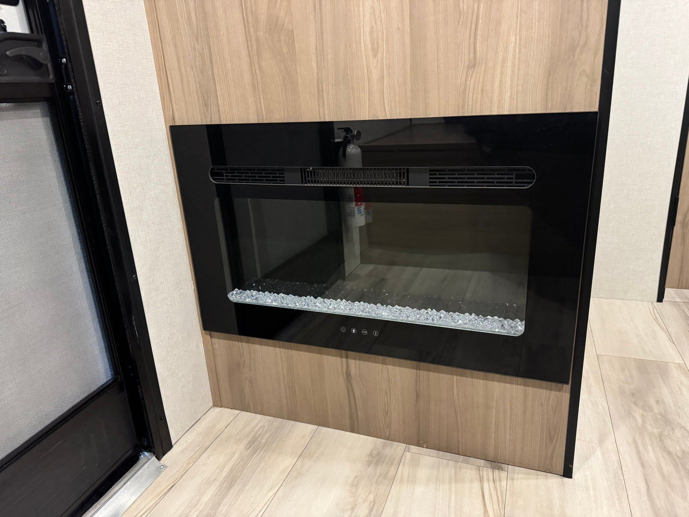 Modern electric fireplace with crystal embers and light wood paneling, enhancing the cozy interior of this RV rental.