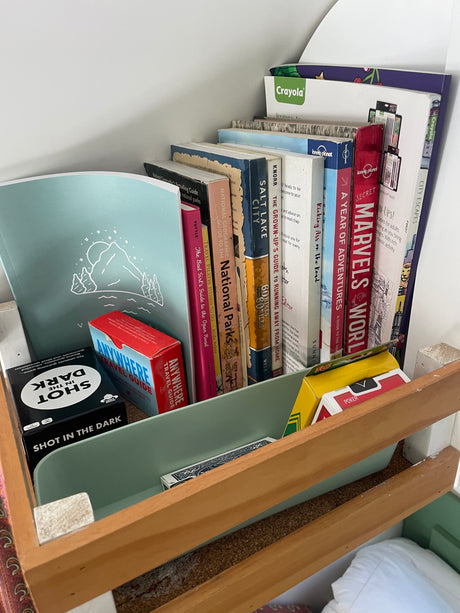 A shelf neatly packed with travel guides, adventure books, card games, and Crayola supplies, ideal for an RV rental adventure.