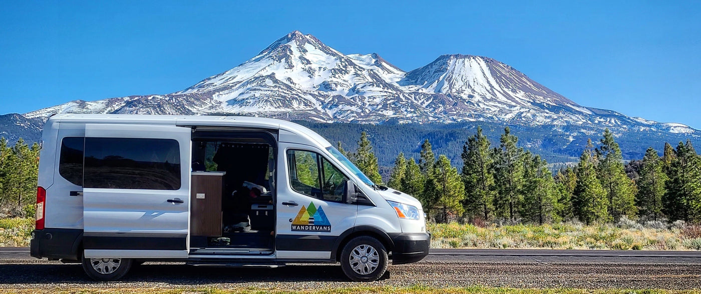 White Wandervans RV rental sits by a road, its door open, with majestic snowy mountains and a forest behind. — photo 6