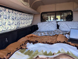 Cozy rv rental interior with a bed, laptop, pillows, and floral curtains, ready for a comfortable camping trip.