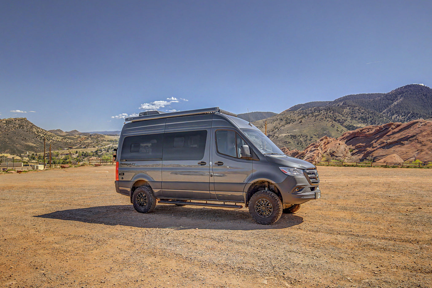 Off-road RV rental: A rugged Mercedes Sprinter adventure van in a scenic mountain landscape with red rocks, parked on a dirt lot.