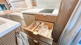 Compact RV rental kitchen: sleek design, organized storage with open drawer of utensils & containers. Perfect for mobile living.