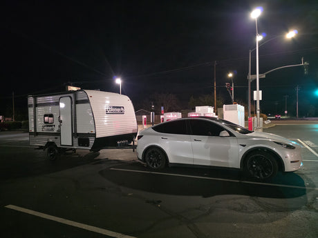 Tesla Model Y towing a Coleman RV rental camper at a night Supercharger stop. Adventure awaits!