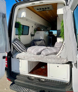 RV rental: Cozy camper van interior with bed, storage cabinets, and natural light from the open back doors.