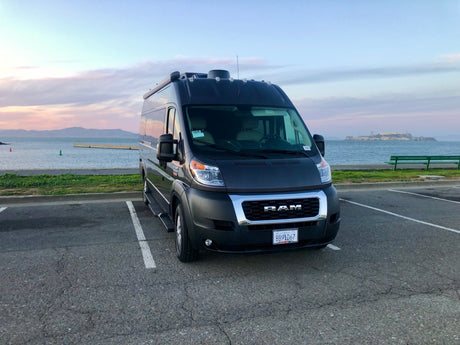 Dark gray Ram ProMaster rv rental by San Francisco Bay, with Alcatraz under a beautiful pastel sky.