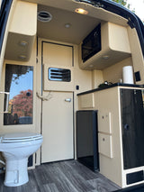 Modern RV rental interior with compact kitchen (microwave, fridge, sink) and a toilet. Beige & wood tones for comfortable travel.