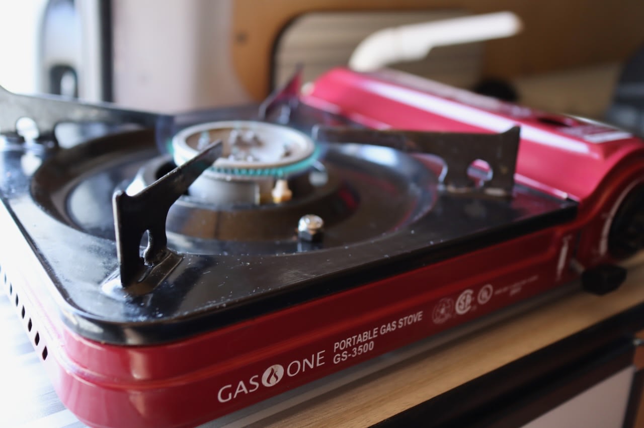 A red portable gas stove, brand Gas One, with a blue flame lit. Essential for cooking on your RV rental road trip.