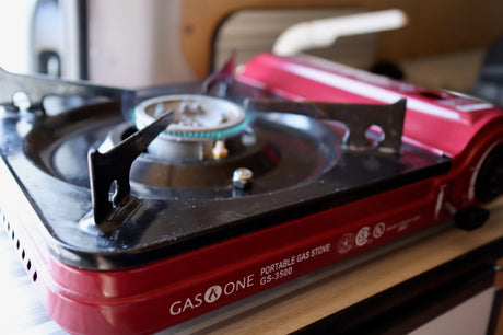A red portable gas stove, brand Gas One, with a blue flame lit. Essential for cooking on your RV rental road trip.