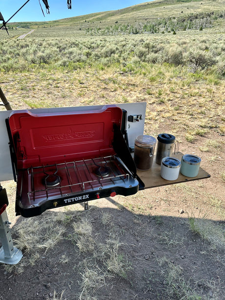 Outdoor cooking with a Teton 2X stove & coffee mugs at an RV rental campsite. Surrounded by sagebrush landscape.