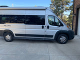 Silver Thor Tellaro RV rental van parked on a concrete driveway by a house, ready for adventure.