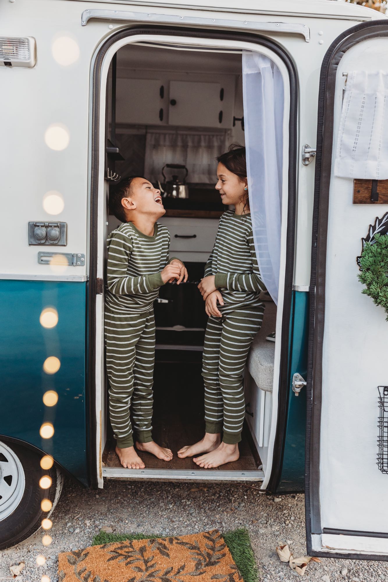 Barefoot kids in striped pajamas giggle inside an RV rental doorway, enjoying cozy camper adventures.