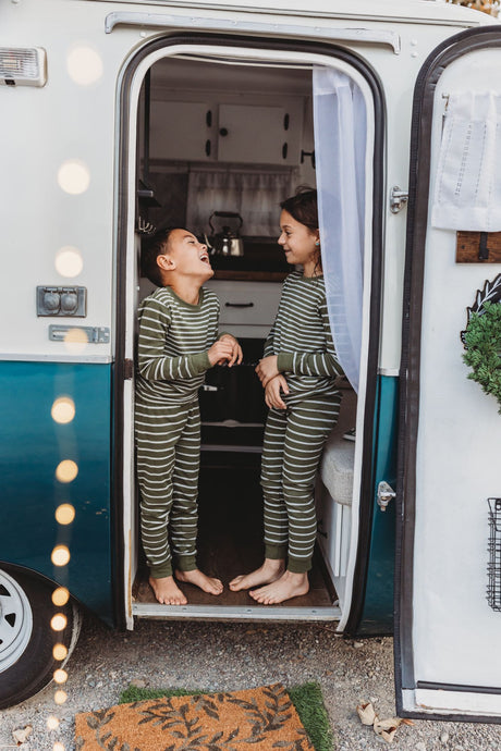 Barefoot kids in striped pajamas giggle inside an RV rental doorway, enjoying cozy camper adventures.