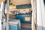 Explore this compact RV rental! A bright camper van interior features a blue kitchen with sink, fridge, and a cozy bed area.