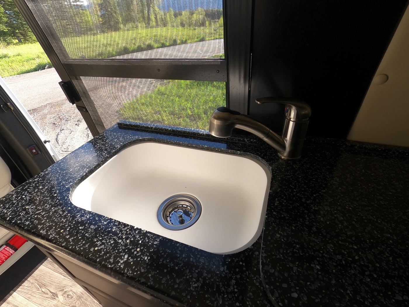 RV rental kitchen: white sink, speckled counter, and faucet, with a view of nature through a screen. — photo 14