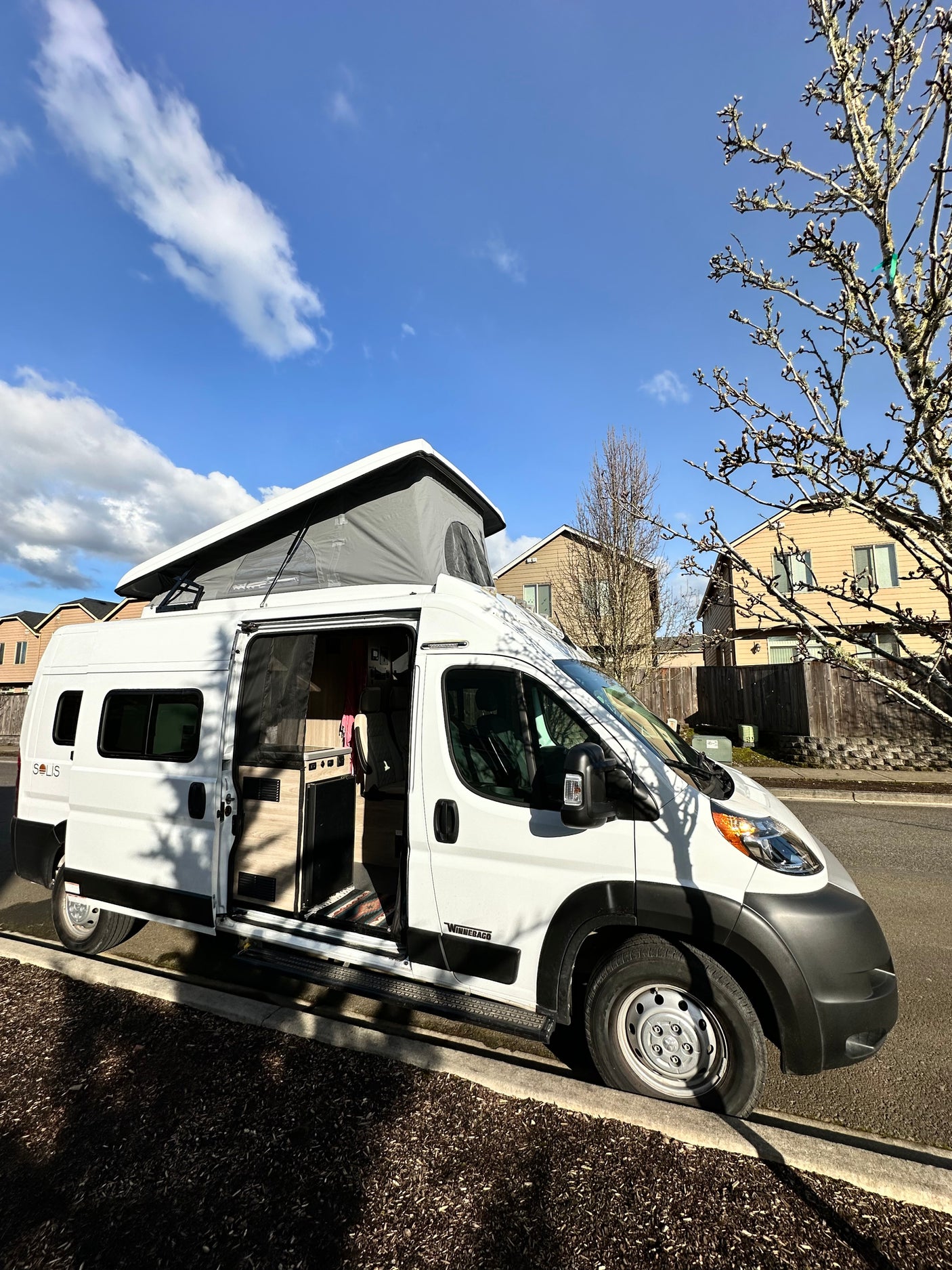 White camper van (Winnebago Solis) with pop-top extended, parked on a residential street. Perfect for an rv rental adventure!