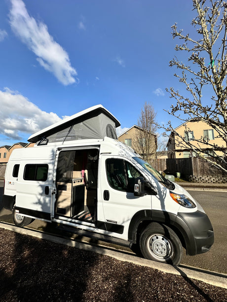 White camper van (Winnebago Solis) with pop-top extended, parked on a residential street. Perfect for an rv rental adventure!