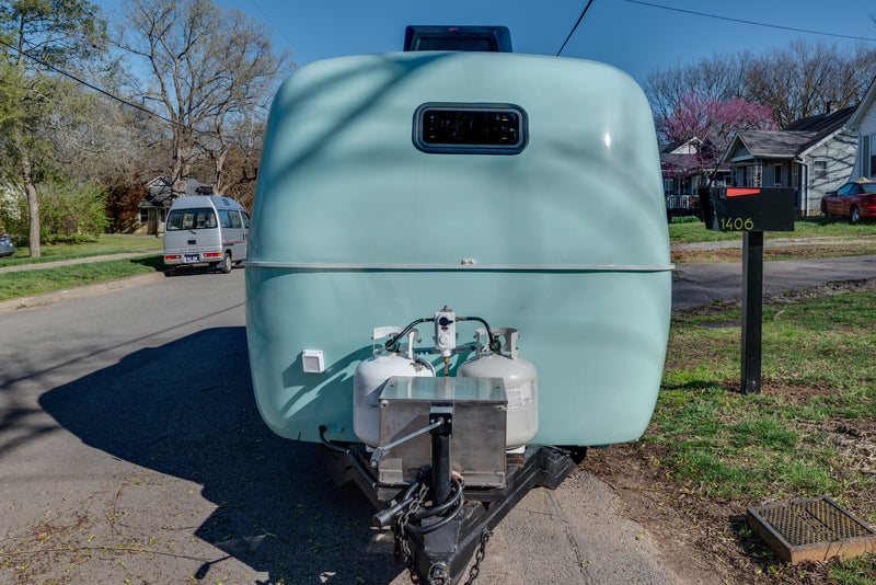 Rounded light blue camper rental with propane tanks on a residential street. A van and mailbox 1406 are visible. — photo 7
