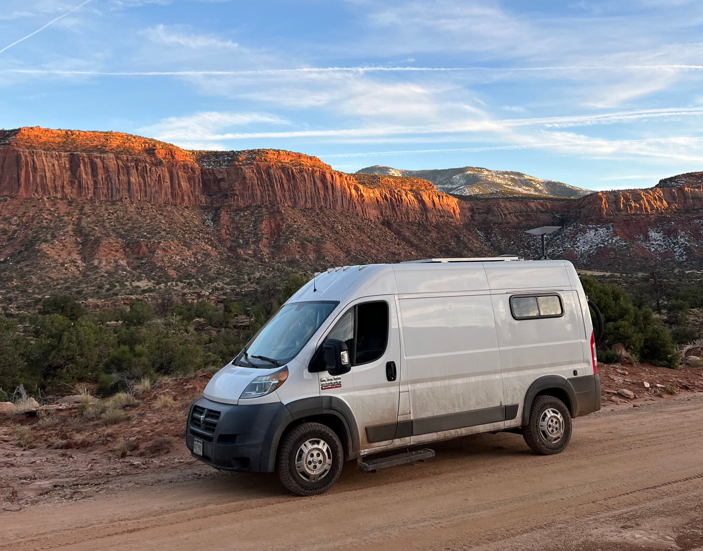 RV rental van on a dirt road, framed by stunning red cliffs and snowy peaks. Perfect for van life exploration.