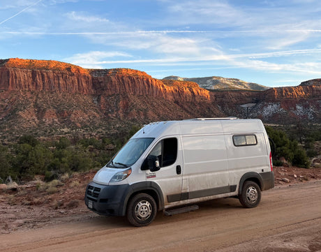 RV rental van on a dirt road, framed by stunning red cliffs and snowy peaks. Perfect for van life exploration.