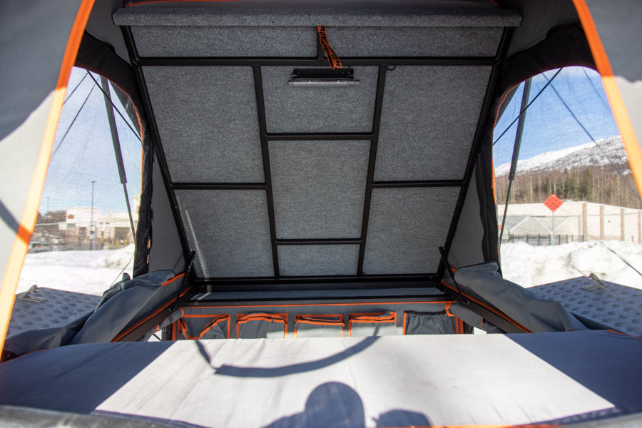 Inside a pop-up rooftop tent, perfect for an RV rental. Features a felt-lined ceiling, integrated light, and organized storage.