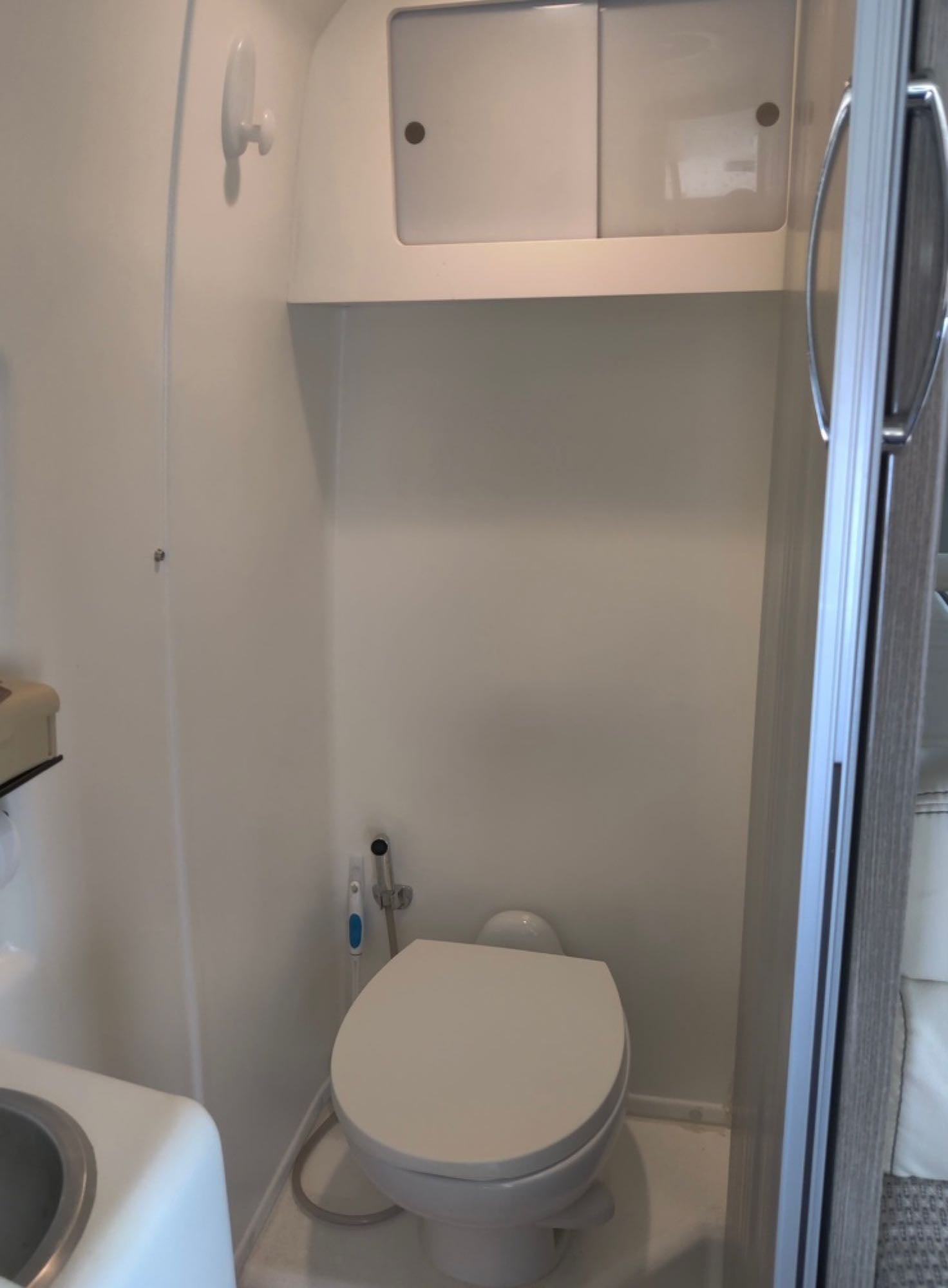 Compact RV rental bathroom featuring a toilet, partial sink, and overhead storage.