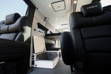 Inside a premium RV rental: Black leather seats face a versatile bed and storage with visible power outlets.