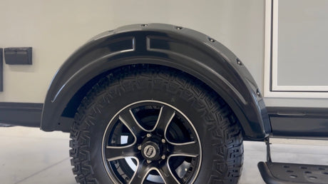 Explore an RV rental's durable exterior: black fender, all-terrain tire on an alloy wheel, utility access, and step.