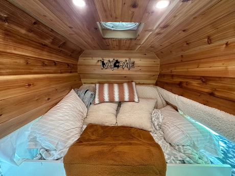Cozy wood-paneled RV rental bedroom, featuring a comfy bed, "WELCOME" sign, and overhead fan.