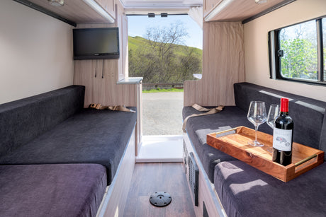 This rv rental offers a comfortable interior with dark upholstered seating, TV, wine setup, and scenic outdoor views.
