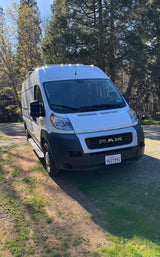 This white Ram ProMaster camper van, available as an rv rental, is ready for adventure amidst tall trees.