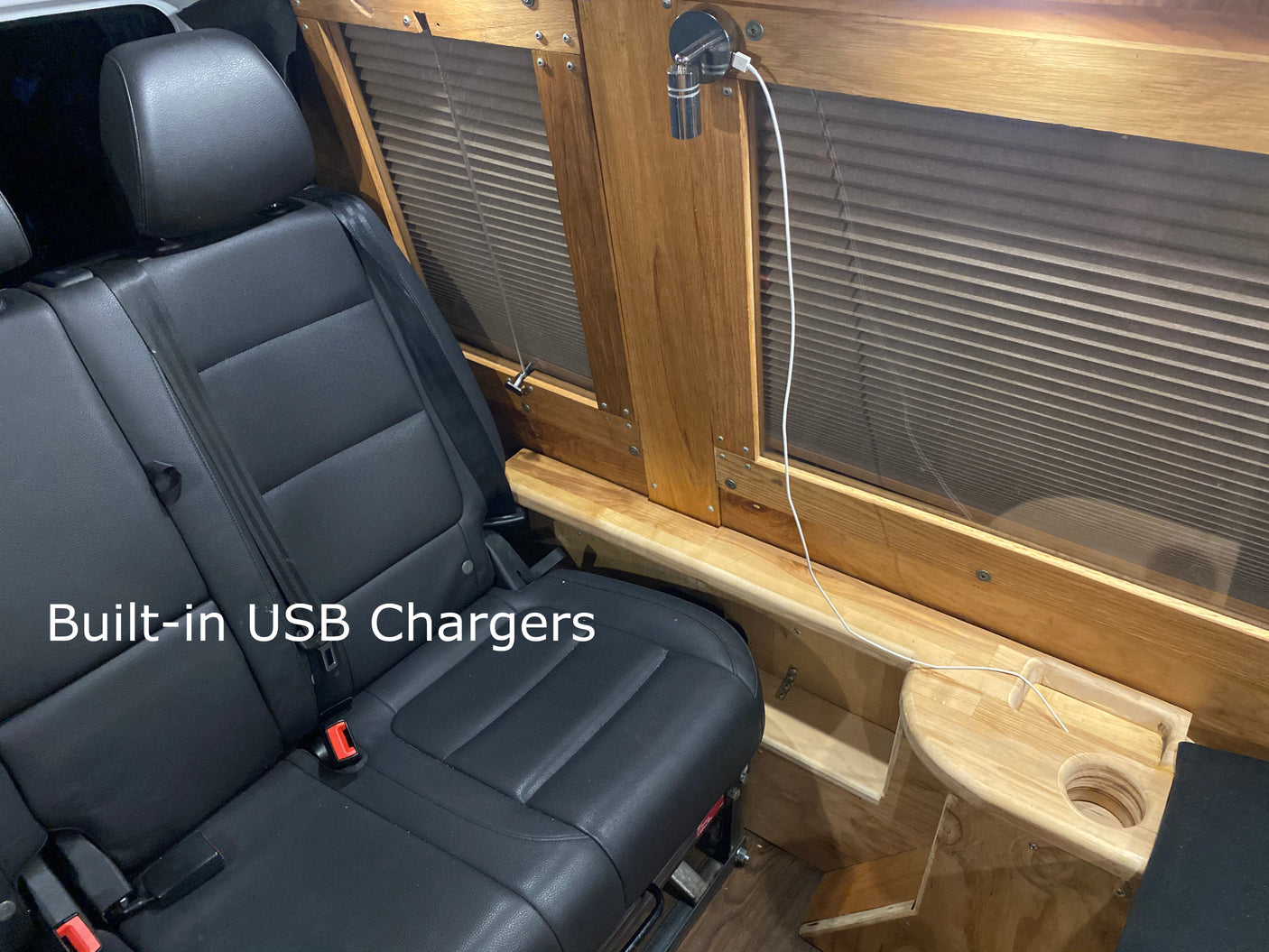 RV rental interior: passenger seat, wooden window trim with integrated USB charger & cupholder for convenience.
