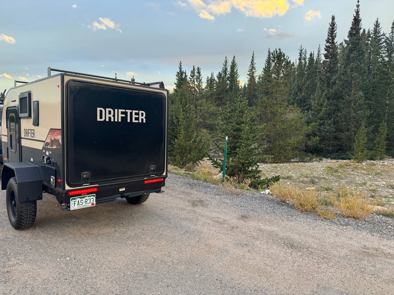 with mountains and trees in the background. Perfect for your camping adventure.|A "Drifter" off-road camper trailer is parked on a gravel path — photo 2