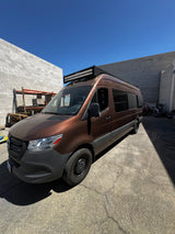 Customized brown Mercedes Sprinter van with a roof light bar, ready for RV rental adventures under blue skies.