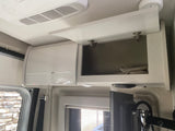 RV rental interior showcasing overhead storage cabinets (one open), ceiling AC, TV, and window with blind. Compact and organized.