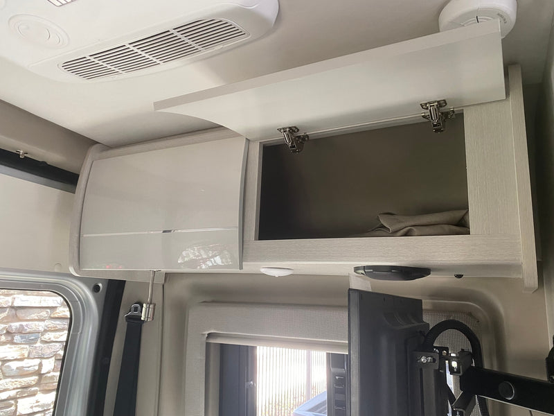 RV rental interior showcasing overhead storage cabinets (one open), ceiling AC, TV, and window with blind. Compact and organized. — photo 11