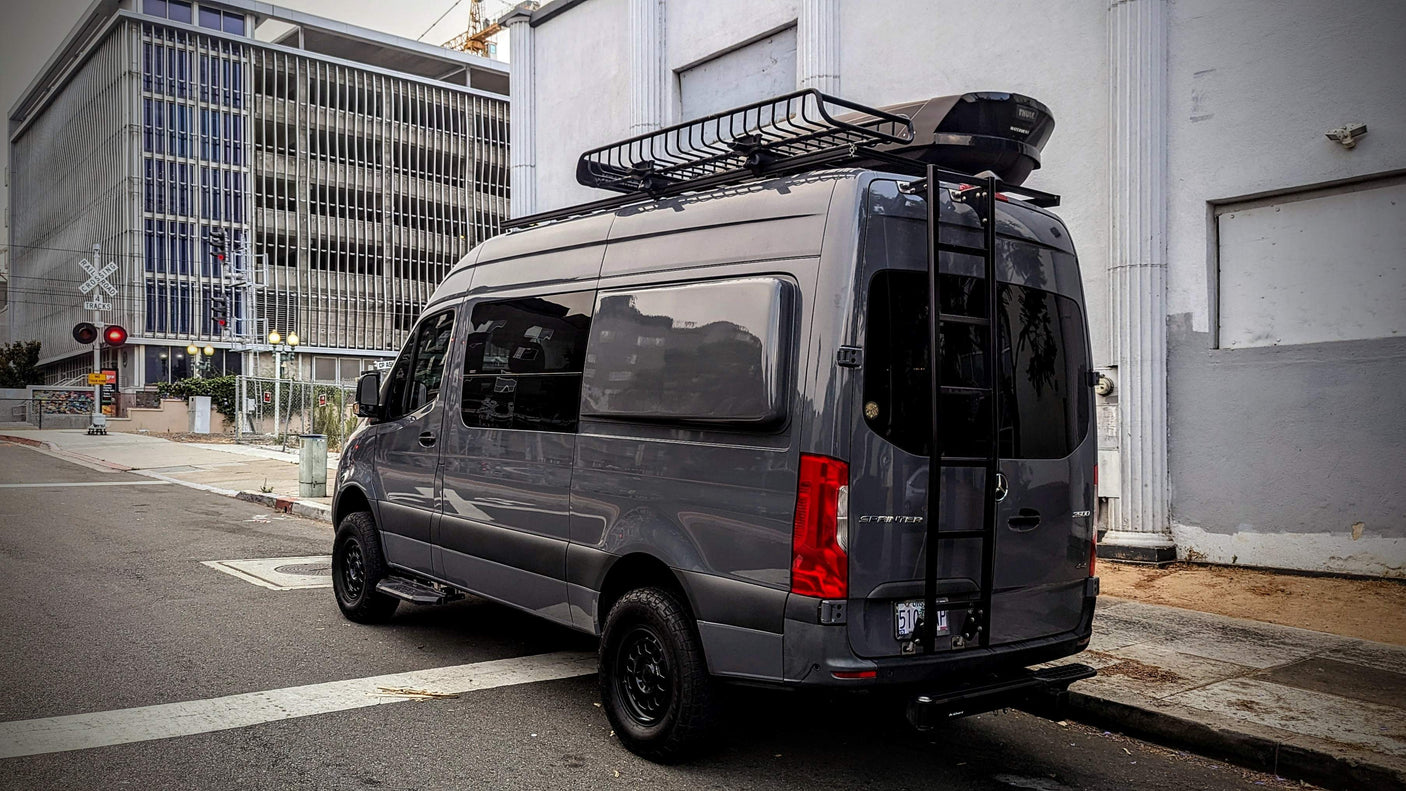 Dark gray Sprinter RV rental. This custom van features a roof rack, large Thule cargo box, and rear access ladder.