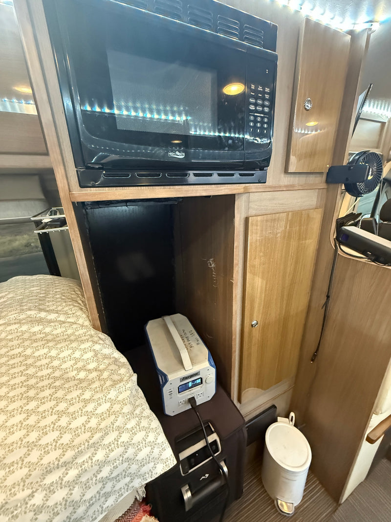 RV rental interior: A compact space with a microwave, cozy bed, and portable power station, highlighting practical amenities. — photo 18