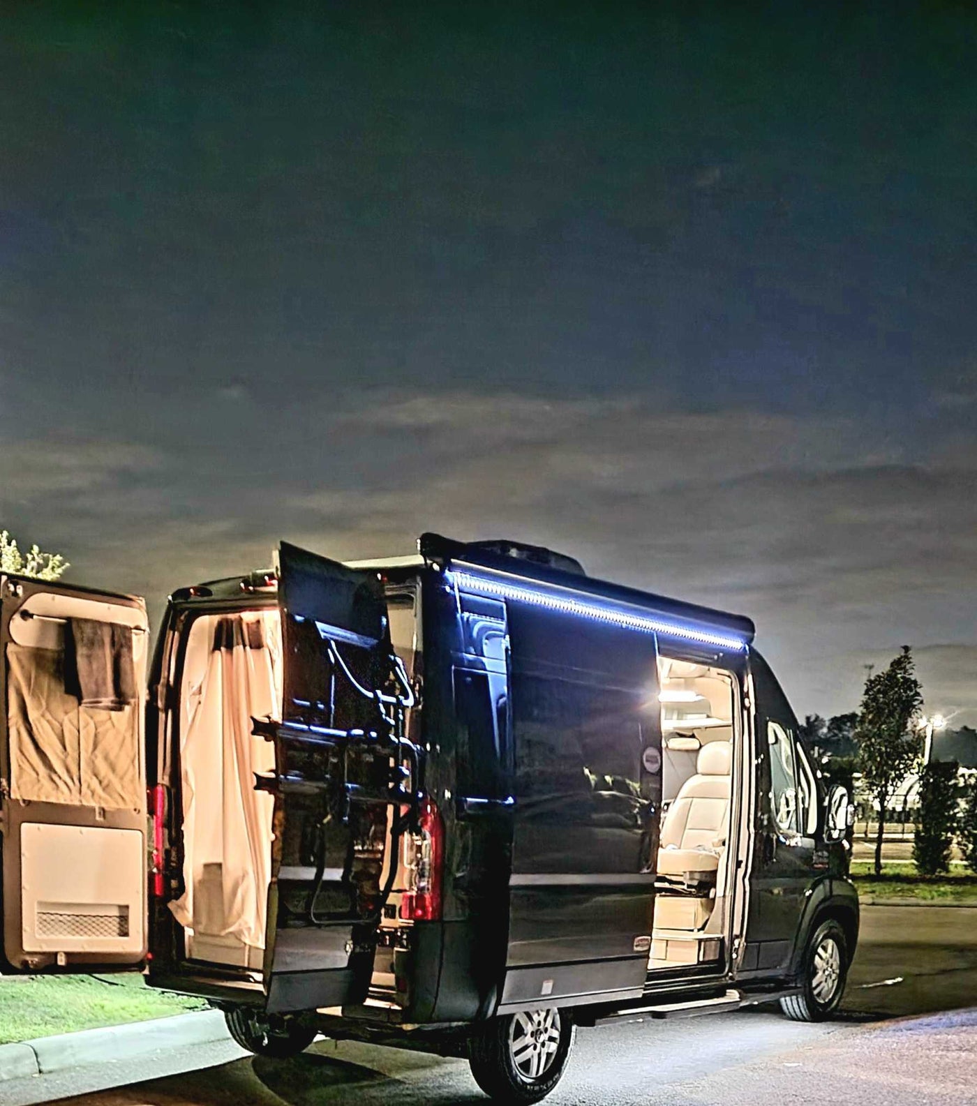 Night shot of an illuminated black RV rental with open doors, revealing a spacious, comfortable interior. Ready for adventure! — photo 13
