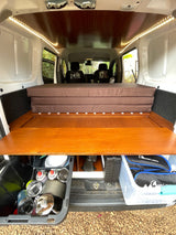 Compact RV rental interior featuring a folded bed, wooden platform, LED lighting, and under-bed camping gear storage.