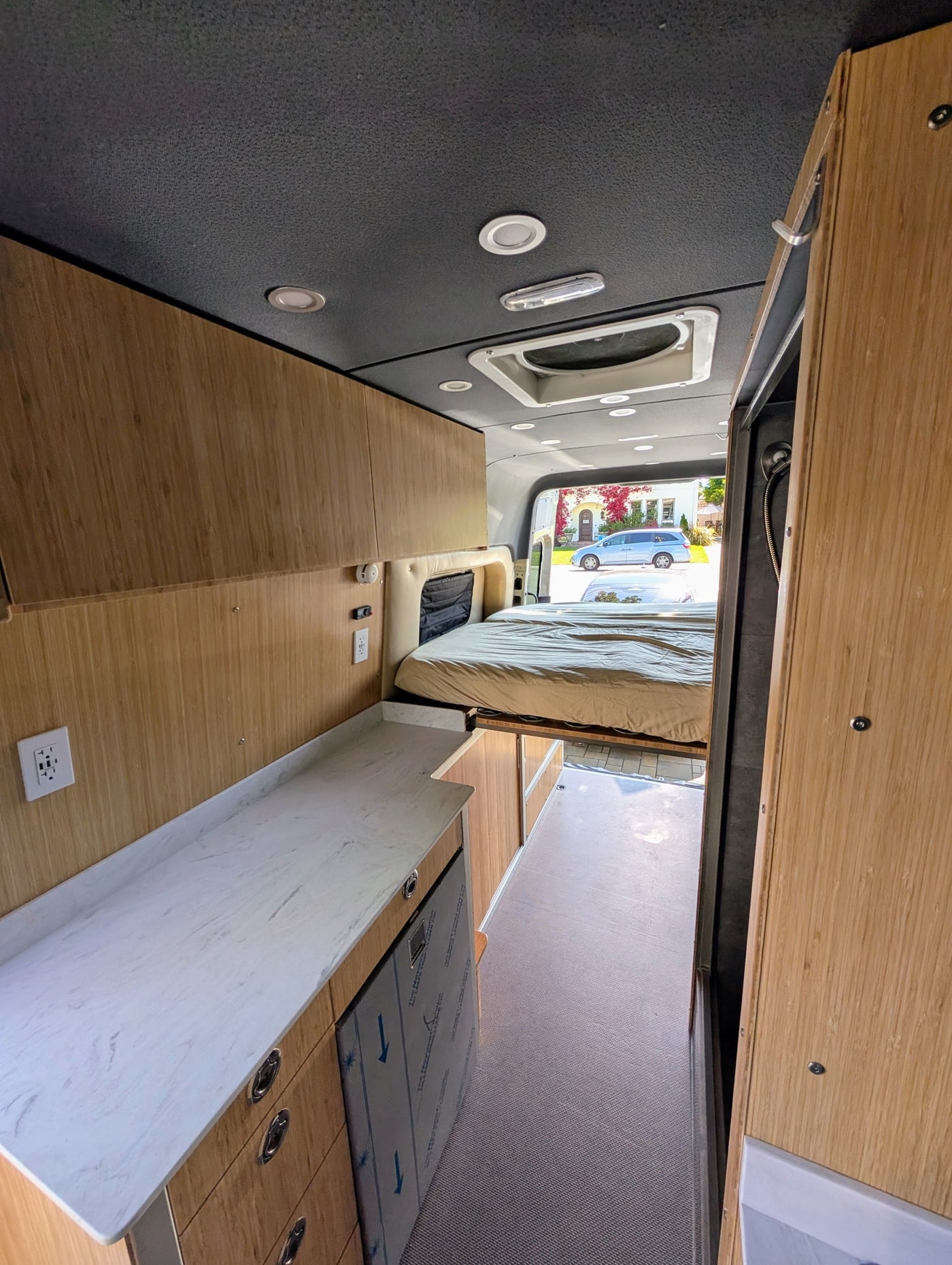 Modern camper van RV rental interior: light wood, kitchen counter, refrigerator, and a cozy bed setup. — photo 5