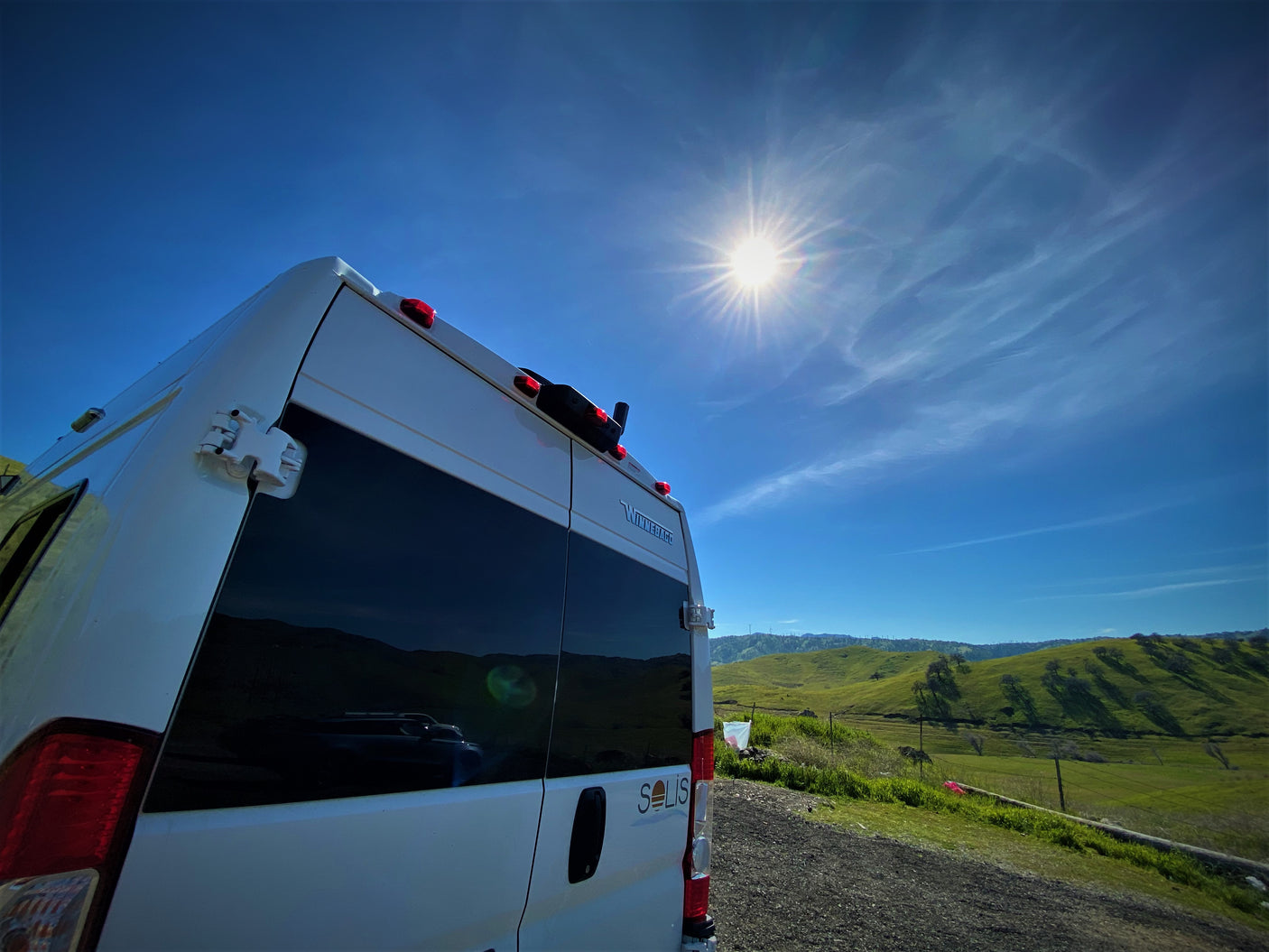 Winnebago Solis RV rental parked in a vibrant green landscape under a brilliant sunny blue sky.