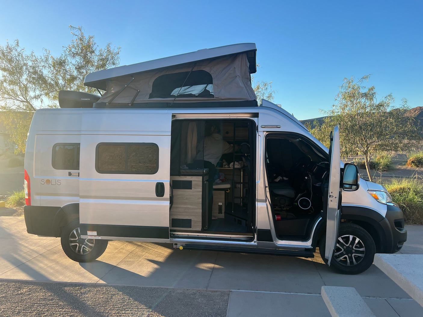 This Winnebago Solis RV rental shows its pop-top extended & side door open, revealing the cozy interior, ready for adventure.