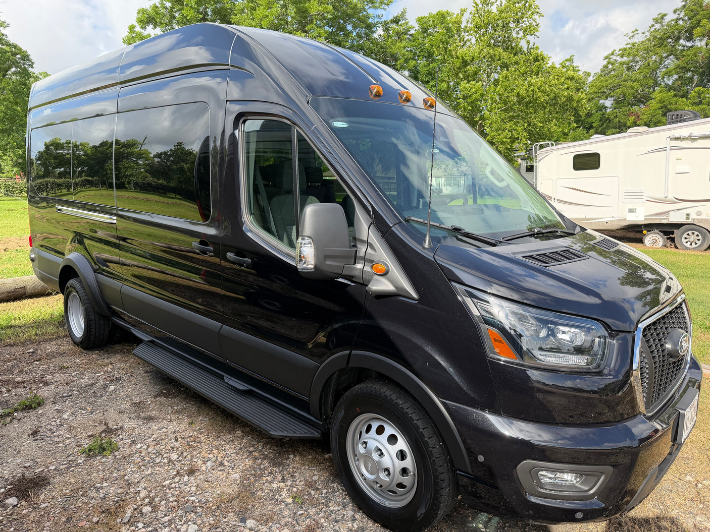 Stylish black Ford Transit van, suitable for rv rental adventures, parked near a white RV amidst trees.