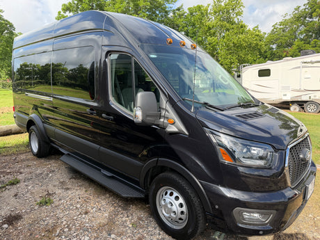 Stylish black Ford Transit van, suitable for rv rental adventures, parked near a white RV amidst trees.